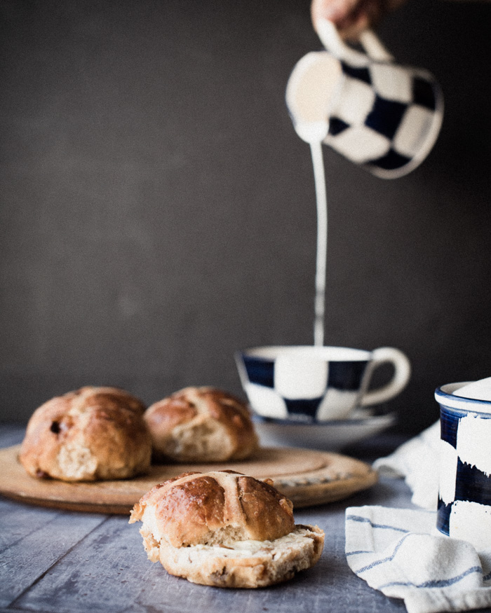 milk pouring from jug into a tea cup and hot cross buns