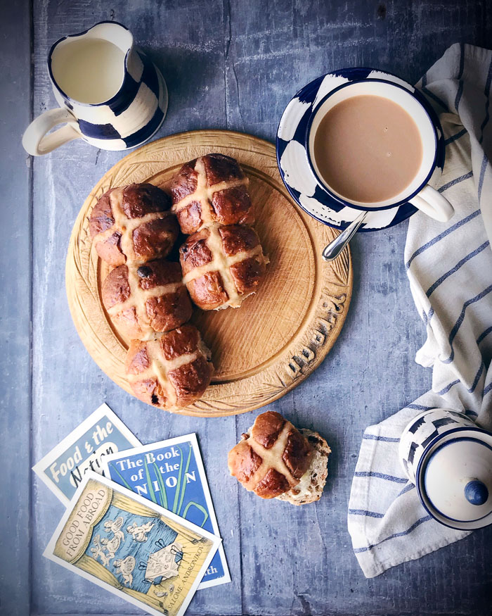 hot cross buns on a board with a cup of tea