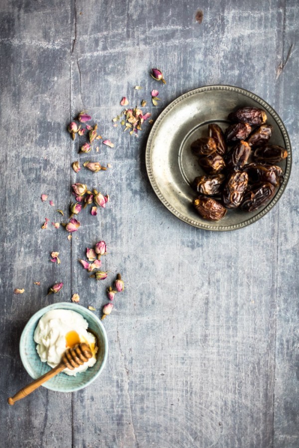 A bowl of dates, some rose buds and yoghurt with a honey drizzler