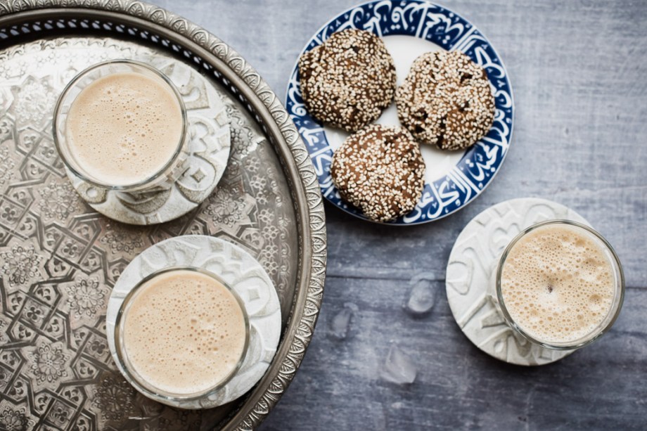 three glasses of date lassi on a tray with a plate of biscuits
