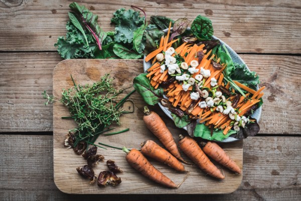 A chopping board with carrots, herbs, dates and a plate of date and carrot salad