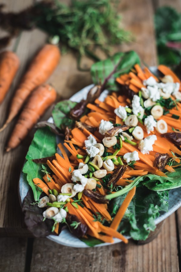 A chopping board with carrots, herbs and a plate of date and carrot salad