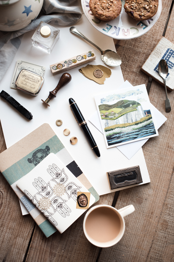 Pens, paper and notebooks for writing a newsletter plus teapot, tea and muffins