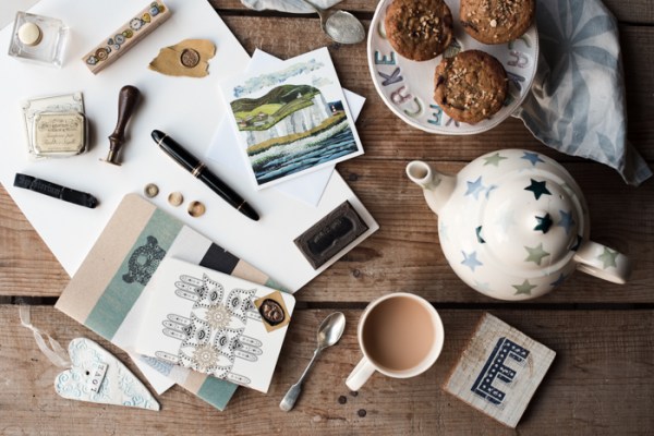 Pens, paper and notebooks for writing a newsletter plus teapot, tea and muffins