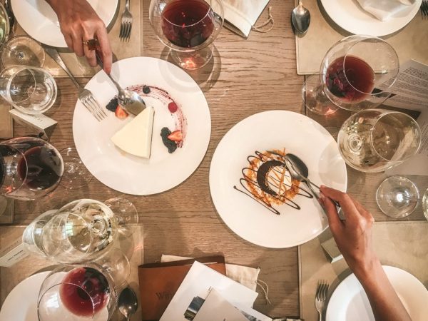 hands reaching over a table with spoons for dessert