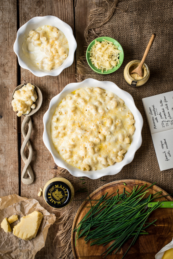 Two bowls of mustard macaroni cheese with a serving spoon
