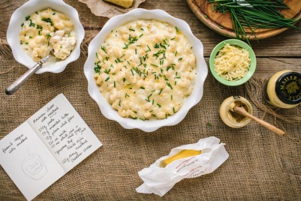 Two bowls of mustard macaroni cheese with a serving spoon