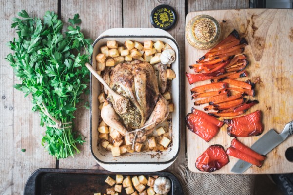 roast chicken with mustard and parsley on a board with red peppers