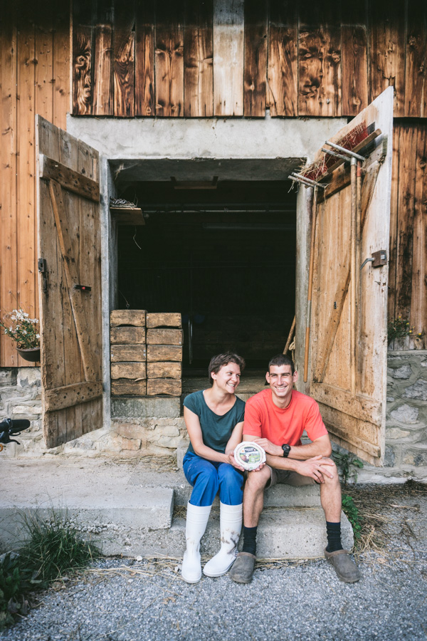 Cheesemakers holding a cheese in front of cowshed